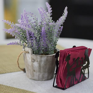 sprig of purple flowers in a glass alongside red napkins